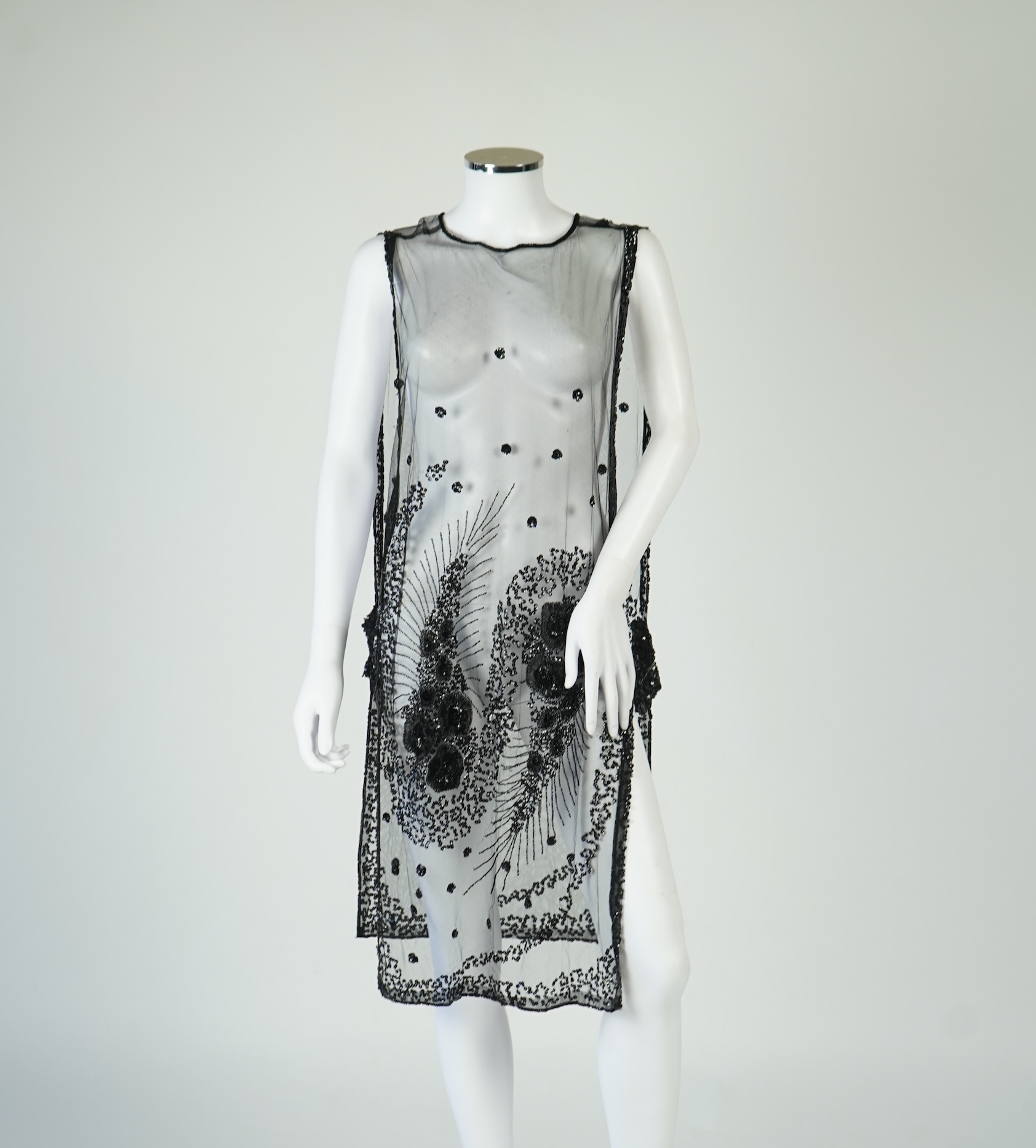 A 1920's black sequin on net tabard, with floral decoration and two side sequinned straps. Length 97cm. Condition - a few sequins have detached but are in a bag for re-attaching.